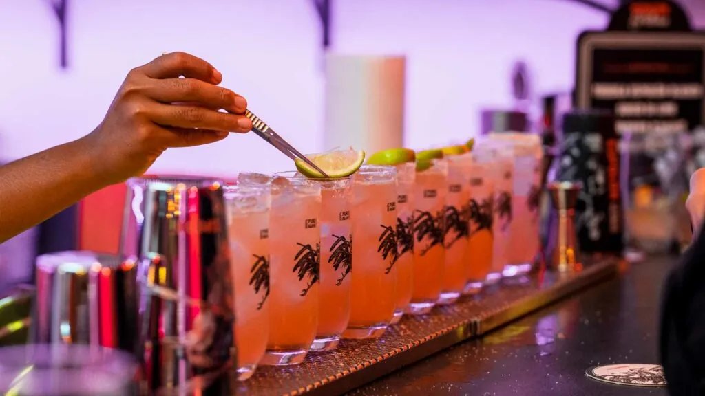 Bartender guarnisce con lime una fila di cocktail Paloma a base di Espolón Tequila